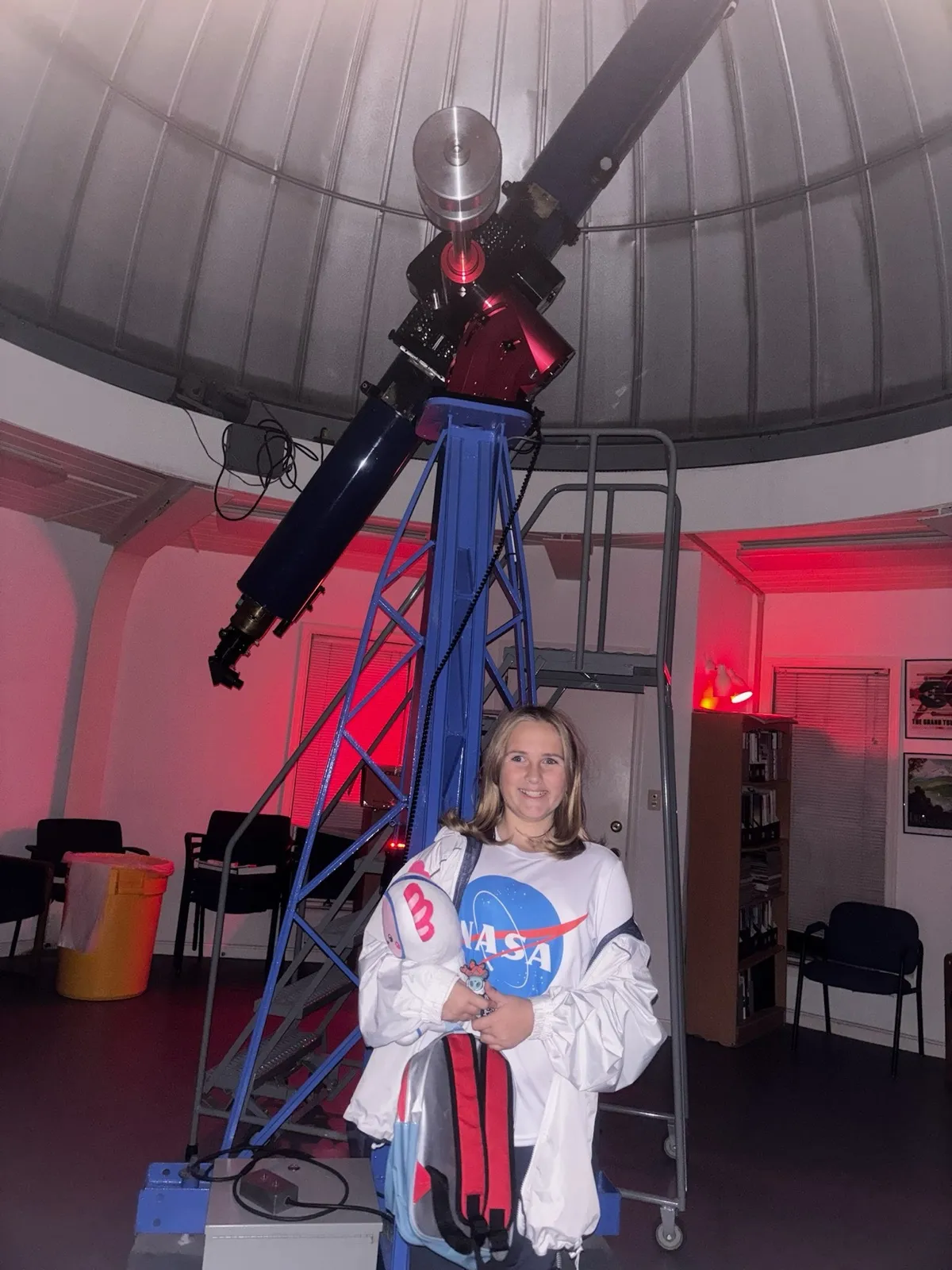 Kenzie inside an observatory standing in front of a large research telescope
